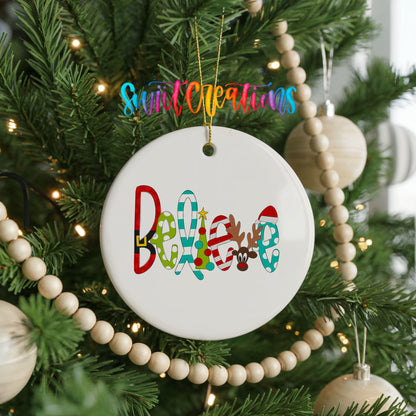 Round ceramic Christmas ornament featuring colorful whimsical Believe holiday lettering, hanging on a decorated Christmas tree