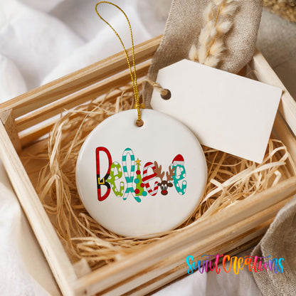 Round ceramic Christmas ornament featuring colorful whimsical Believe holiday lettering, presented in a rustic wooden gift crate