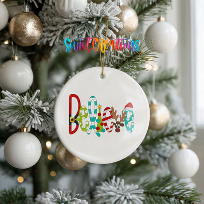 Round ceramic Christmas ornament featuring colorful whimsical Believe holiday lettering, hanging on a frosted holiday tree
