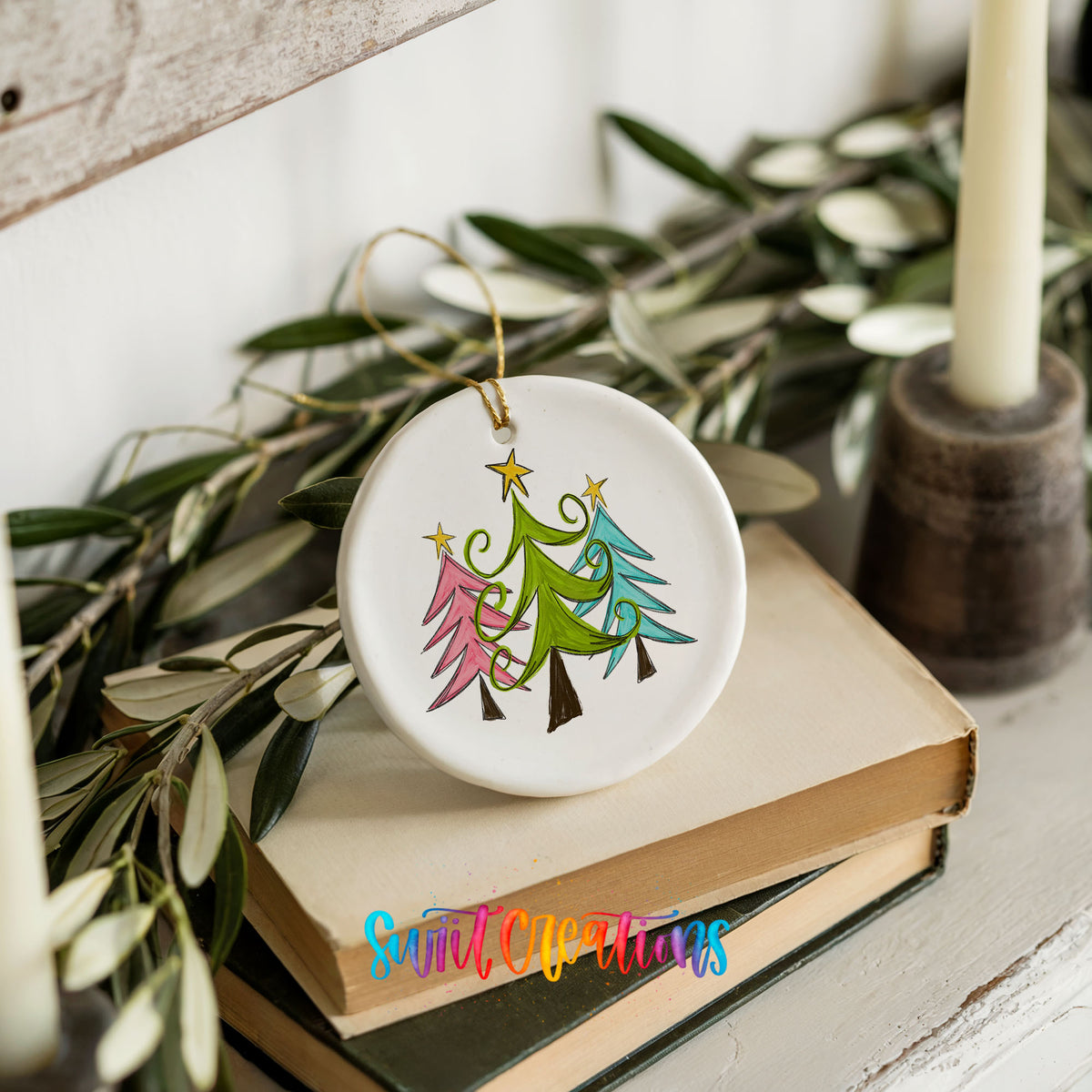 Round ceramic Christmas ornament featuring three colorful whimsical Christmas trees, styled on books with holiday greenery