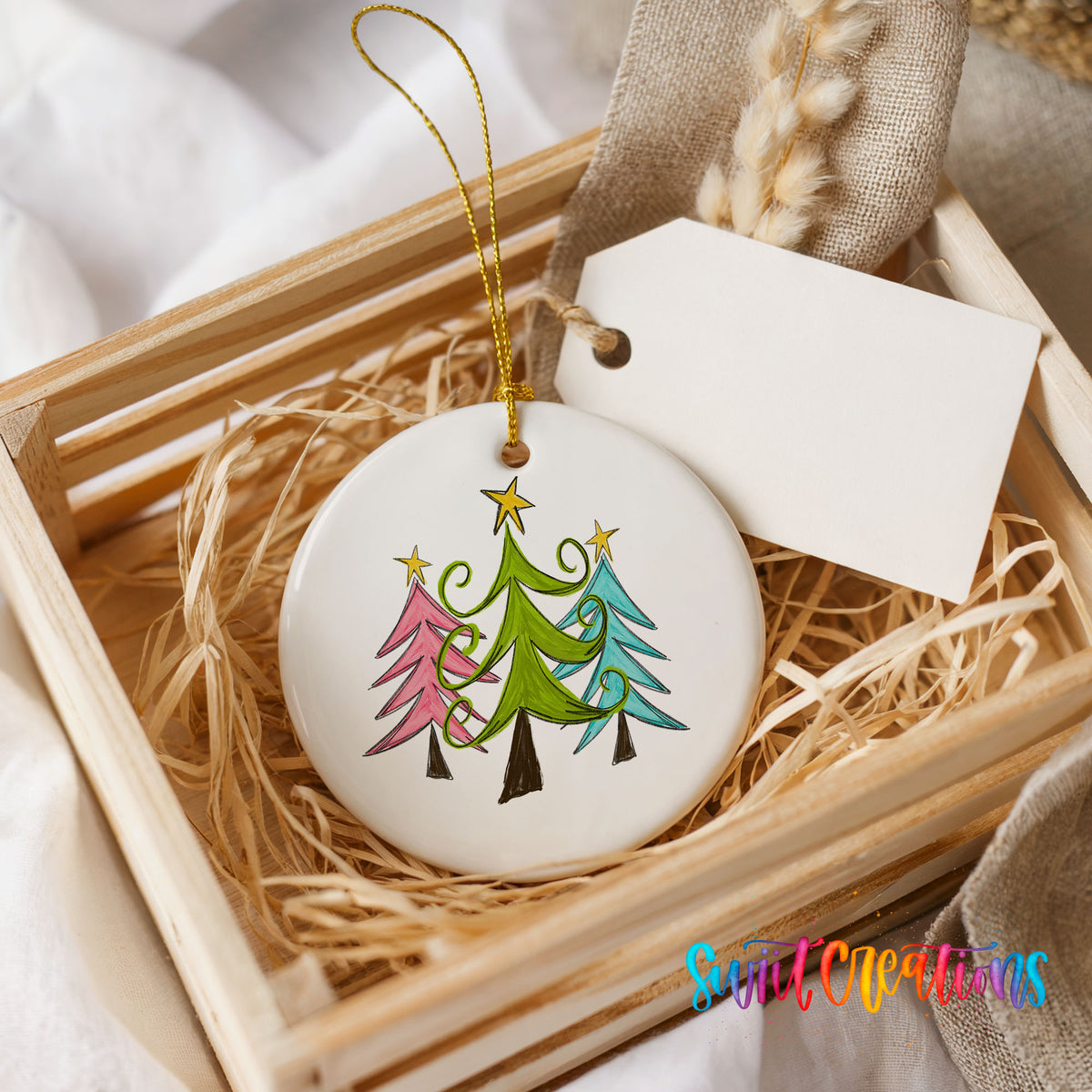 Round ceramic Christmas ornament featuring three colorful whimsical Christmas trees, presented in a rustic wooden gift crate