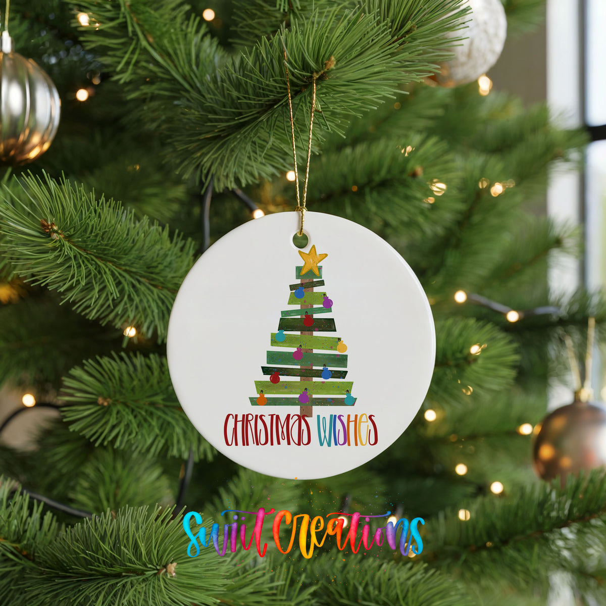 Round ceramic Christmas ornament featuring colorful pallet-style Christmas tree with Christmas Wishes lettering, hanging on a green Christmas tree