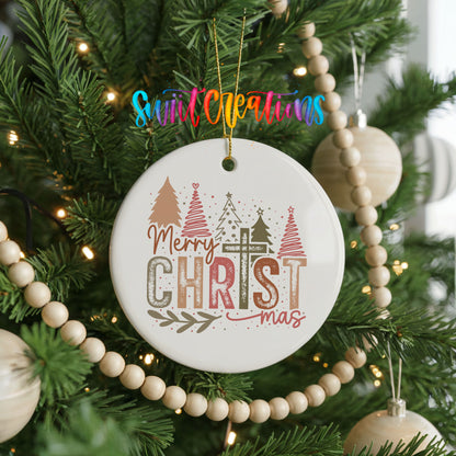 Round ceramic Christmas ornament featuring Merry Christmas typography with a pastel winter village and trees, hanging on a decorated Christmas tree