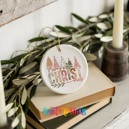 Round ceramic Christmas ornament featuring Merry Christmas typography with a pastel winter village and trees, styled on books with holiday greenery