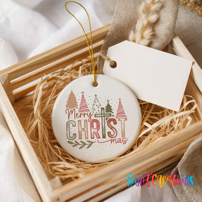 Round ceramic Christmas ornament featuring Merry Christmas typography with a pastel winter village and trees, presented in a rustic wooden gift crate
