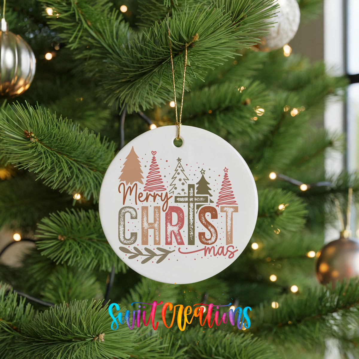 Round ceramic Christmas ornament featuring Merry Christmas typography with a pastel winter village and trees, hanging on a green Christmas tree