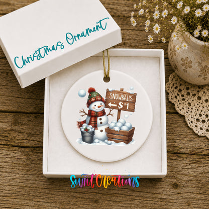 Round ceramic Christmas ornament featuring cheerful snowman selling snowballs for five cents, displayed in the included gift box