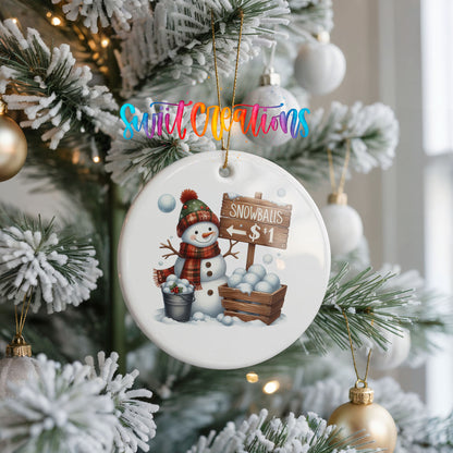 Round ceramic Christmas ornament featuring cheerful snowman selling snowballs for five cents, hanging on a frosted Christmas tree