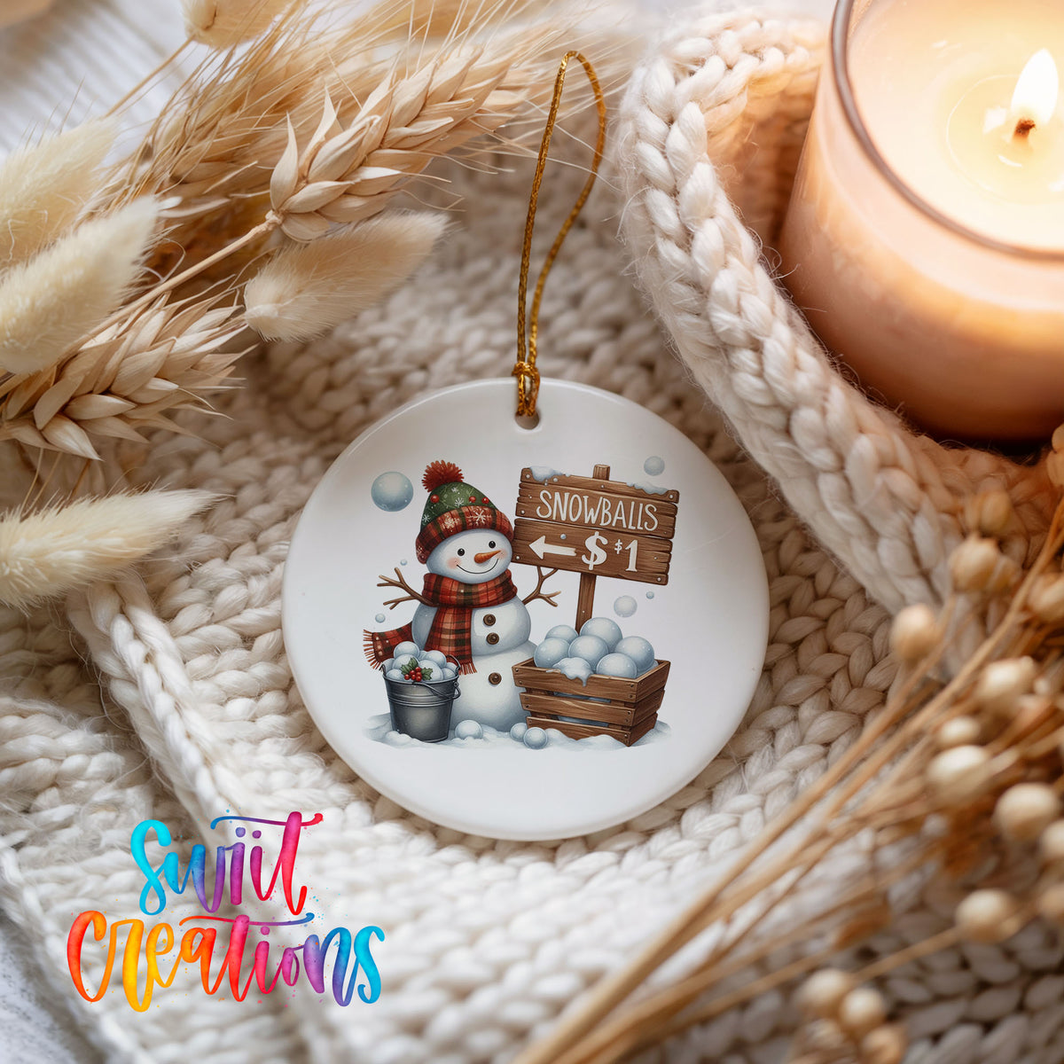 Round ceramic Christmas ornament featuring cheerful snowman selling snowballs for five cents, styled beside a candle and cozy knit blanket