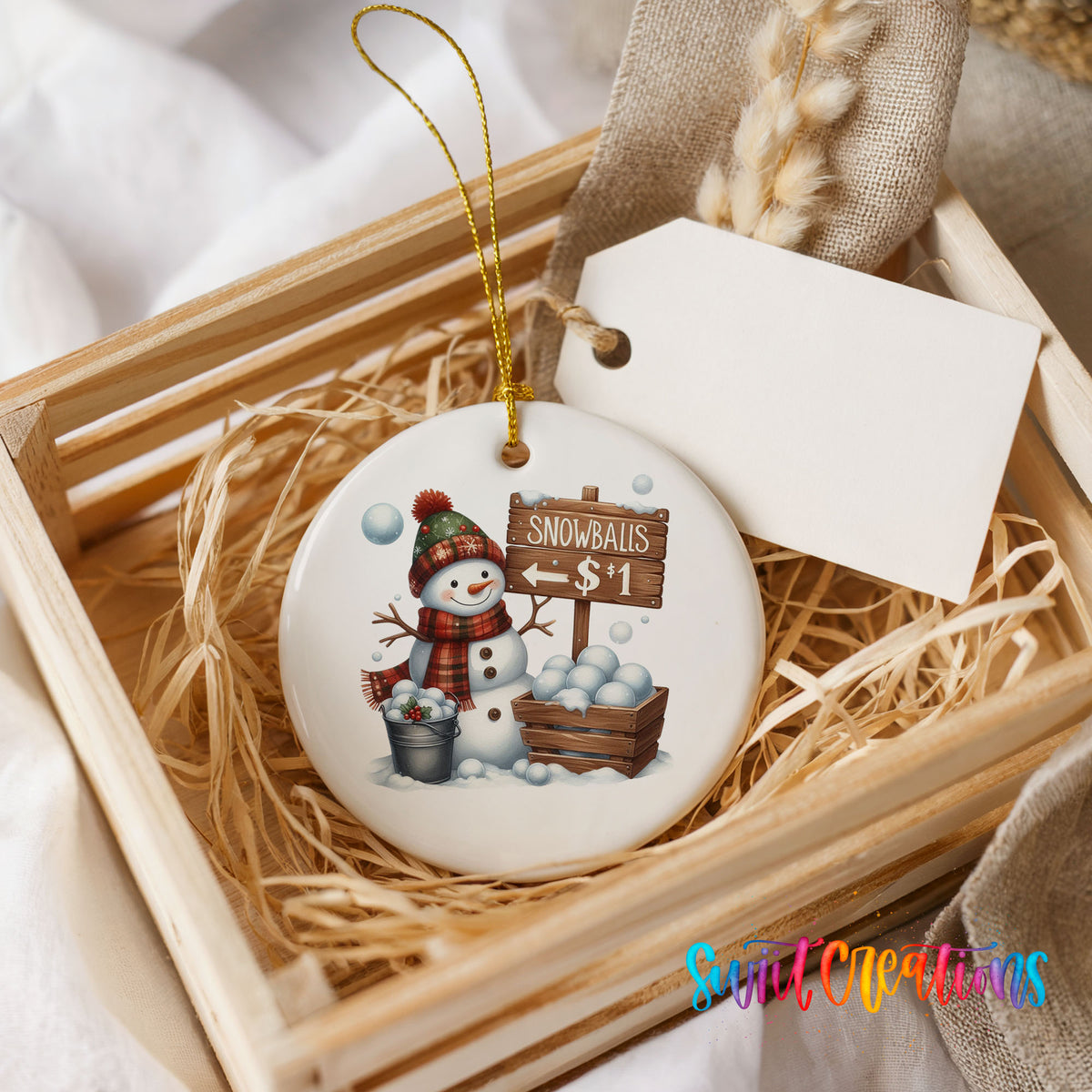 Round ceramic Christmas ornament featuring cheerful snowman selling snowballs for five cents, presented in a rustic wooden gift crate