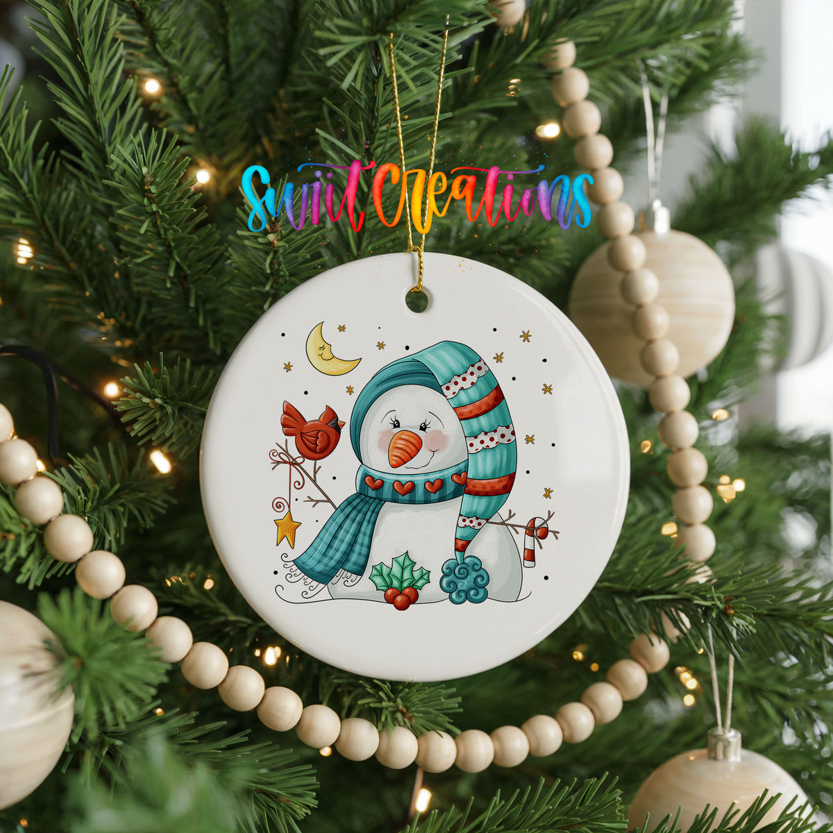 Round ceramic Christmas ornament featuring cozy snowman holding a bright red cardinal beneath a winter moon, hanging on a decorated Christmas tree
