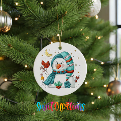 Round ceramic Christmas ornament featuring cozy snowman holding a bright red cardinal beneath a winter moon, hanging on a green Christmas tree