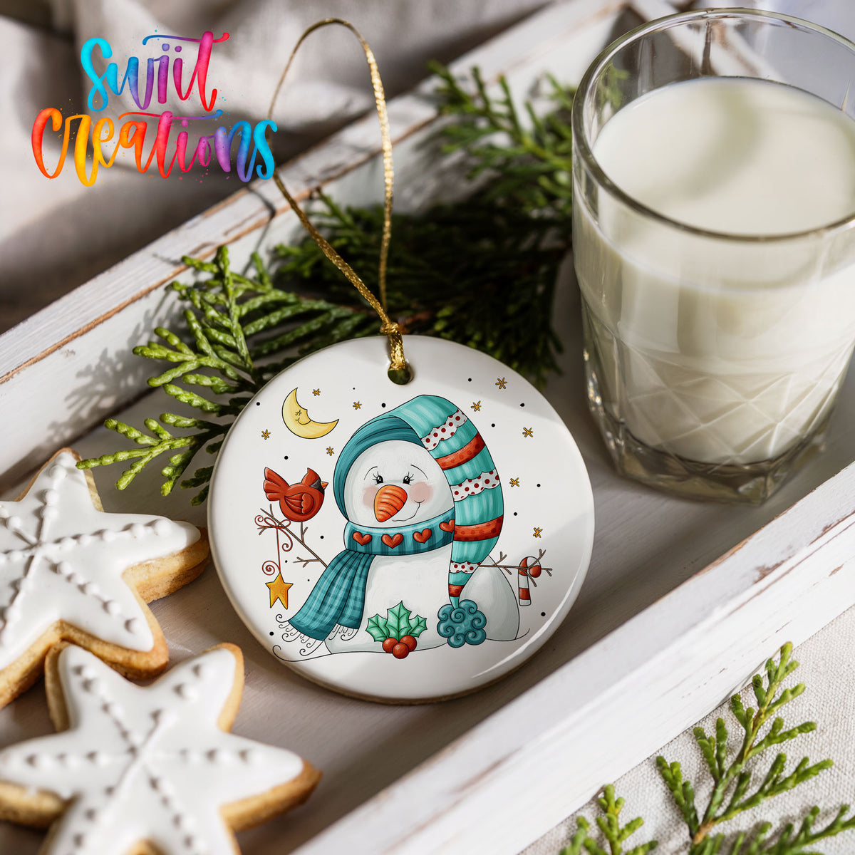Round ceramic Christmas ornament featuring cozy snowman holding a bright red cardinal beneath a winter moon, styled with cookies and milk