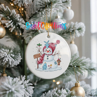 Round ceramic Christmas ornament featuring playful snowman dressed for a colorful winter snow day, hanging on a frosted Christmas tree