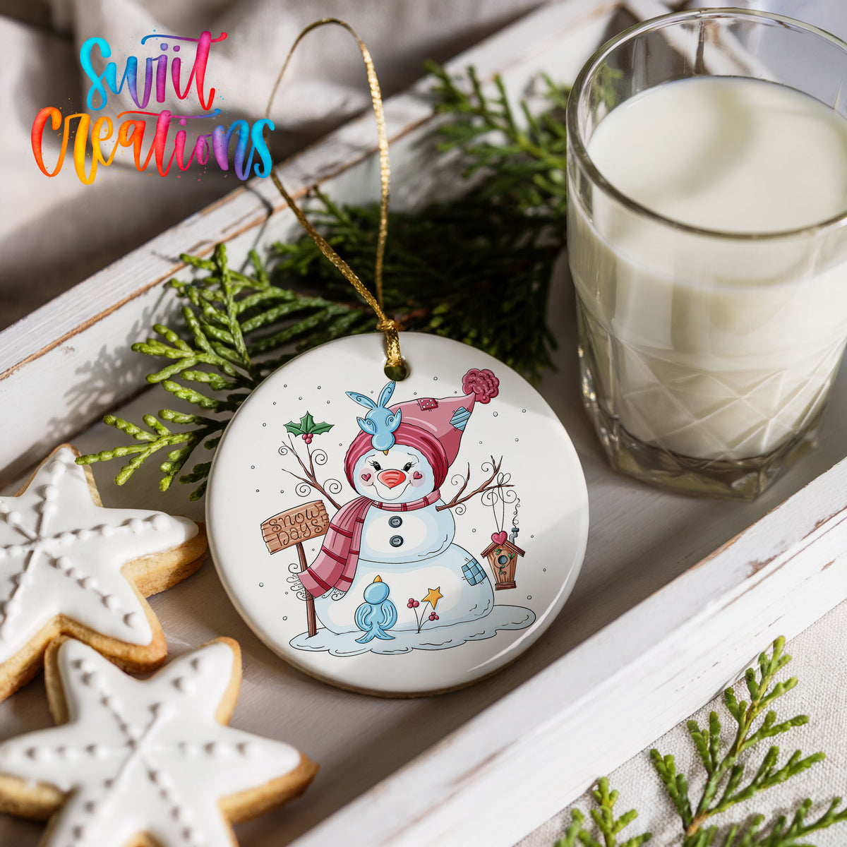 Round ceramic Christmas ornament featuring playful snowman dressed for a colorful winter snow day, styled with cookies and milk