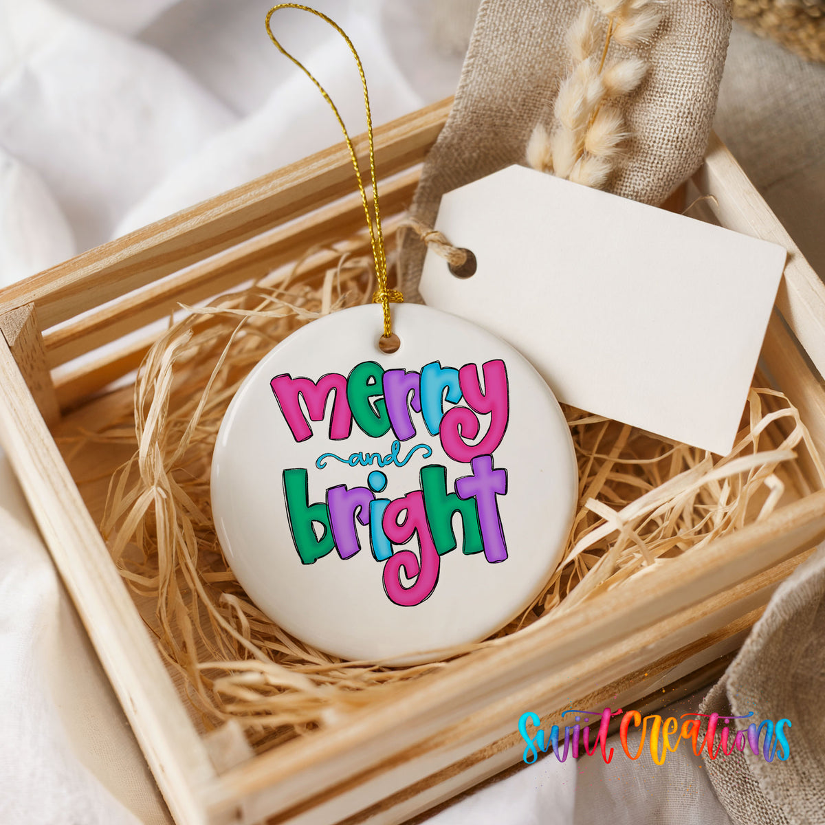 Round ceramic Christmas ornament featuring bright groovy Merry and Bright lettering in pink teal and purple, presented in a rustic wooden gift crate