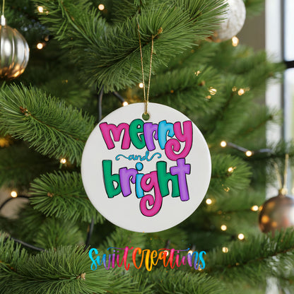 Round ceramic Christmas ornament featuring bright groovy Merry and Bright lettering in pink teal and purple, hanging on a green Christmas tree