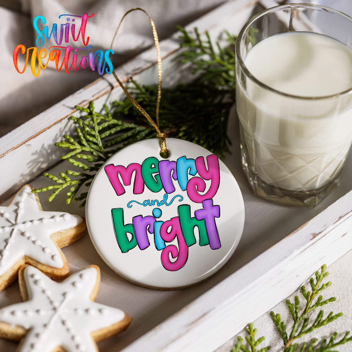 Round ceramic Christmas ornament featuring bright groovy Merry and Bright lettering in pink teal and purple, styled with cookies and milk