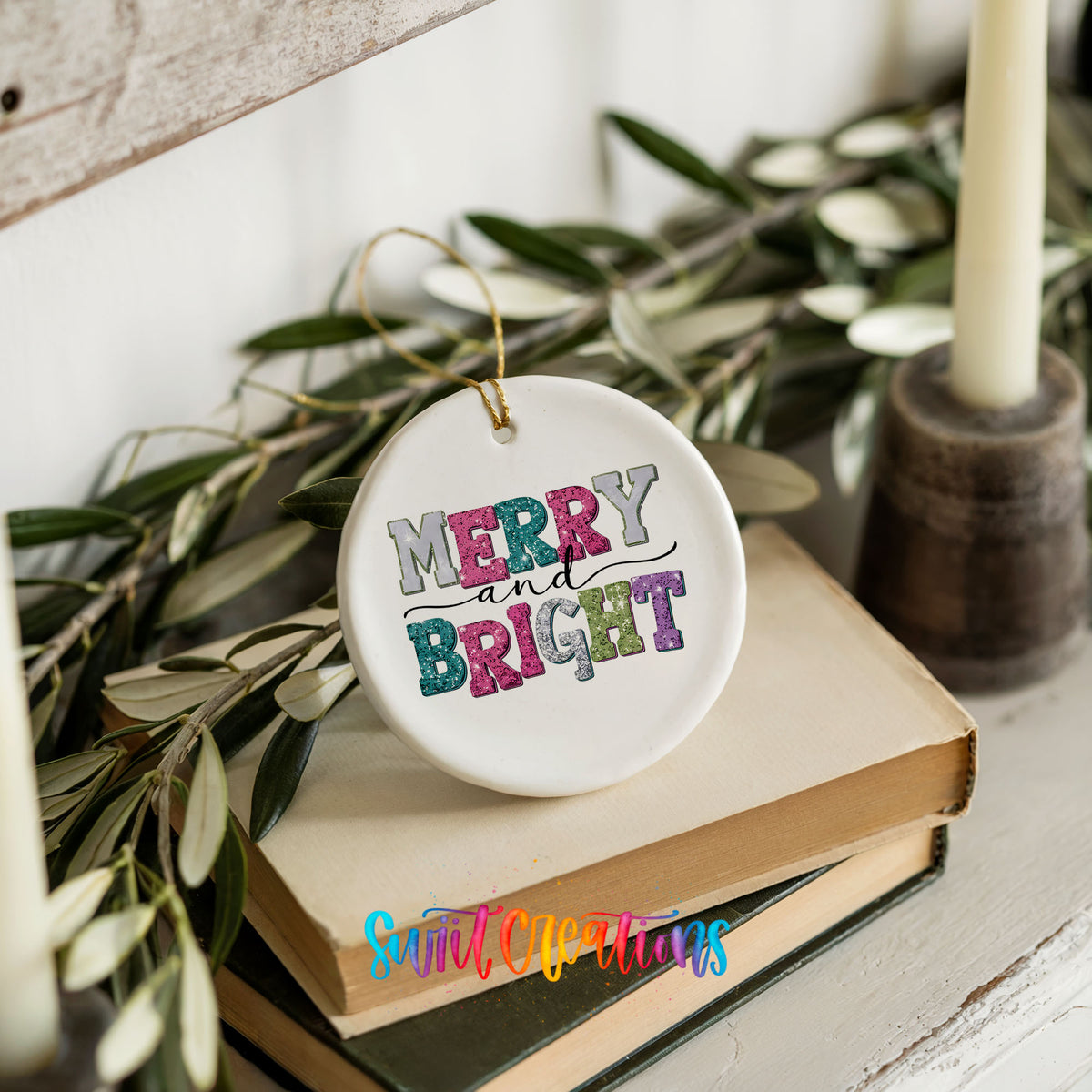 Round ceramic Christmas ornament featuring distressed patchwork Merry and Bright holiday typography, styled on books with holiday greenery