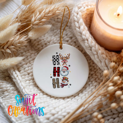 Round ceramic Christmas ornament featuring stacked Ho Ho Ho lettering with cheerful holiday characters, styled beside a candle and cozy knit blanket