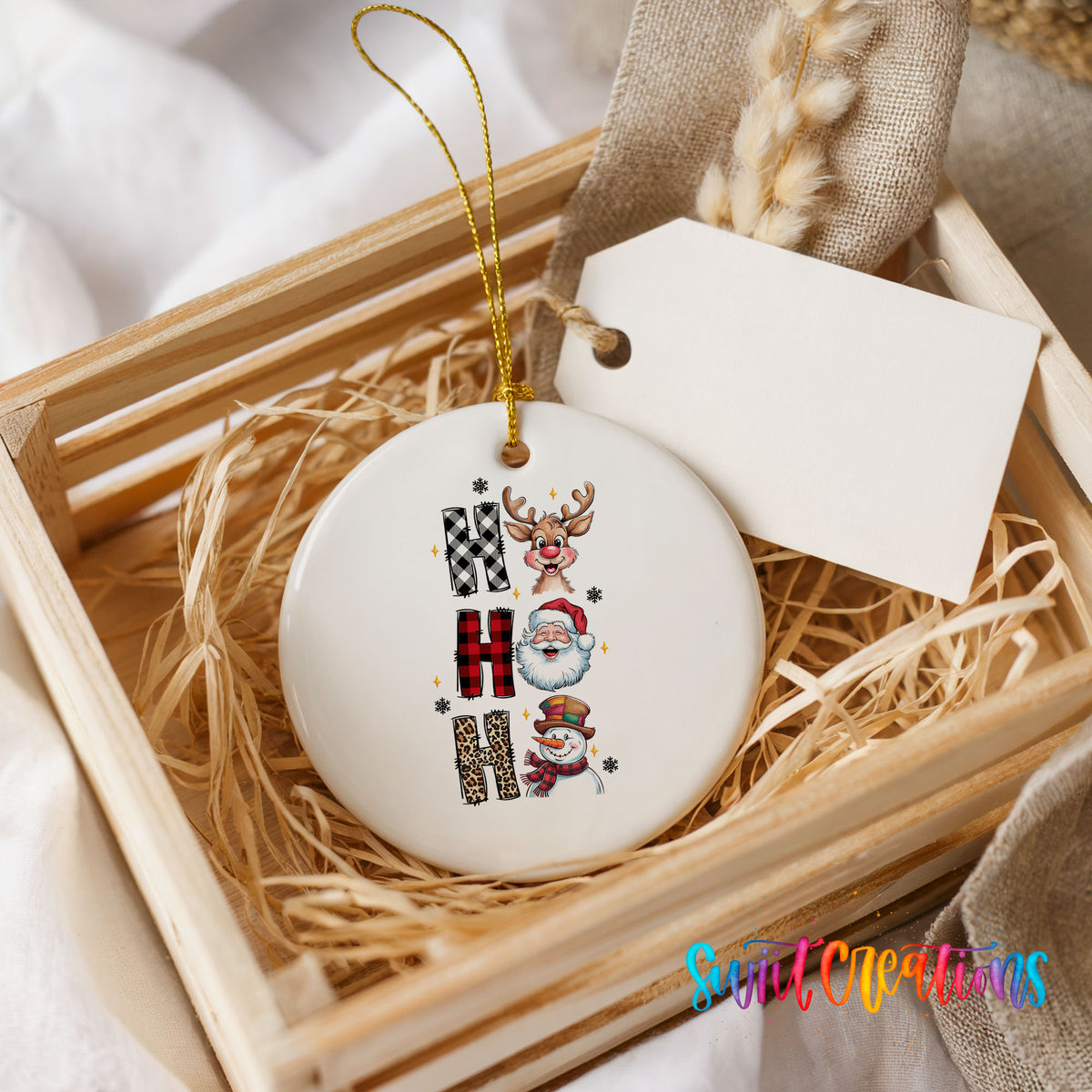 Round ceramic Christmas ornament featuring stacked Ho Ho Ho lettering with cheerful holiday characters, presented in a rustic wooden gift crate