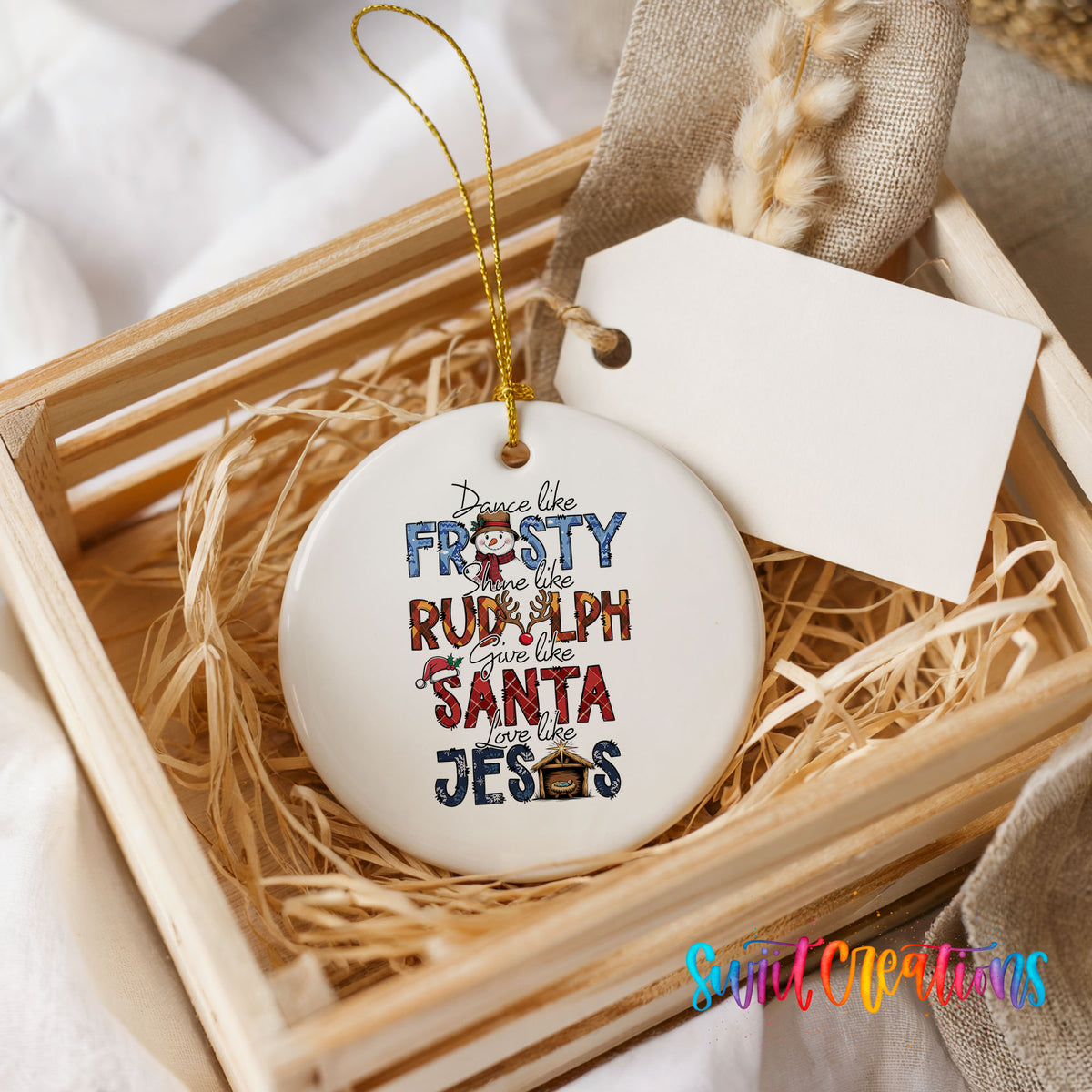 Round ceramic Christmas ornament featuring Dance like Frosty ride like Rudolph give like Santa love like Jesus message, presented in a rustic wooden gift crate