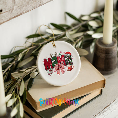 Round ceramic Christmas ornament featuring festive patterned Mama lettering with a large red holiday bow, styled on books with holiday greenery