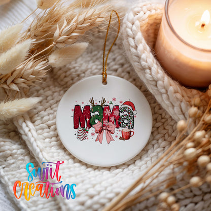 Round ceramic Christmas ornament featuring festive patterned Mama lettering with a large red holiday bow, styled beside a candle and cozy knit blanket