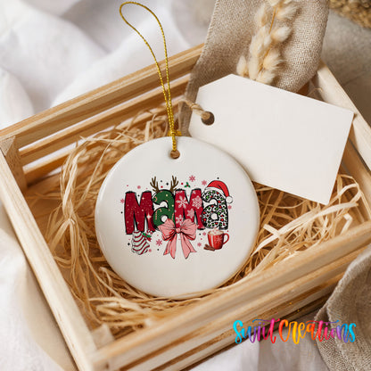 Round ceramic Christmas ornament featuring festive patterned Mama lettering with a large red holiday bow, presented in a rustic wooden gift crate
