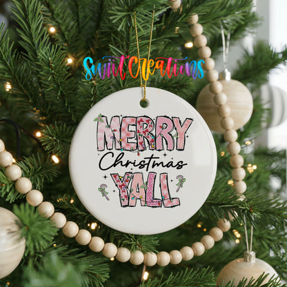 Round ceramic Christmas ornament featuring patterned Merry Christmas Y’all lettering with pink and green accents, hanging on a decorated Christmas tree