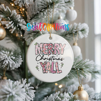 Round ceramic Christmas ornament featuring patterned Merry Christmas Y’all lettering with pink and green accents, hanging on a frosted Christmas tree