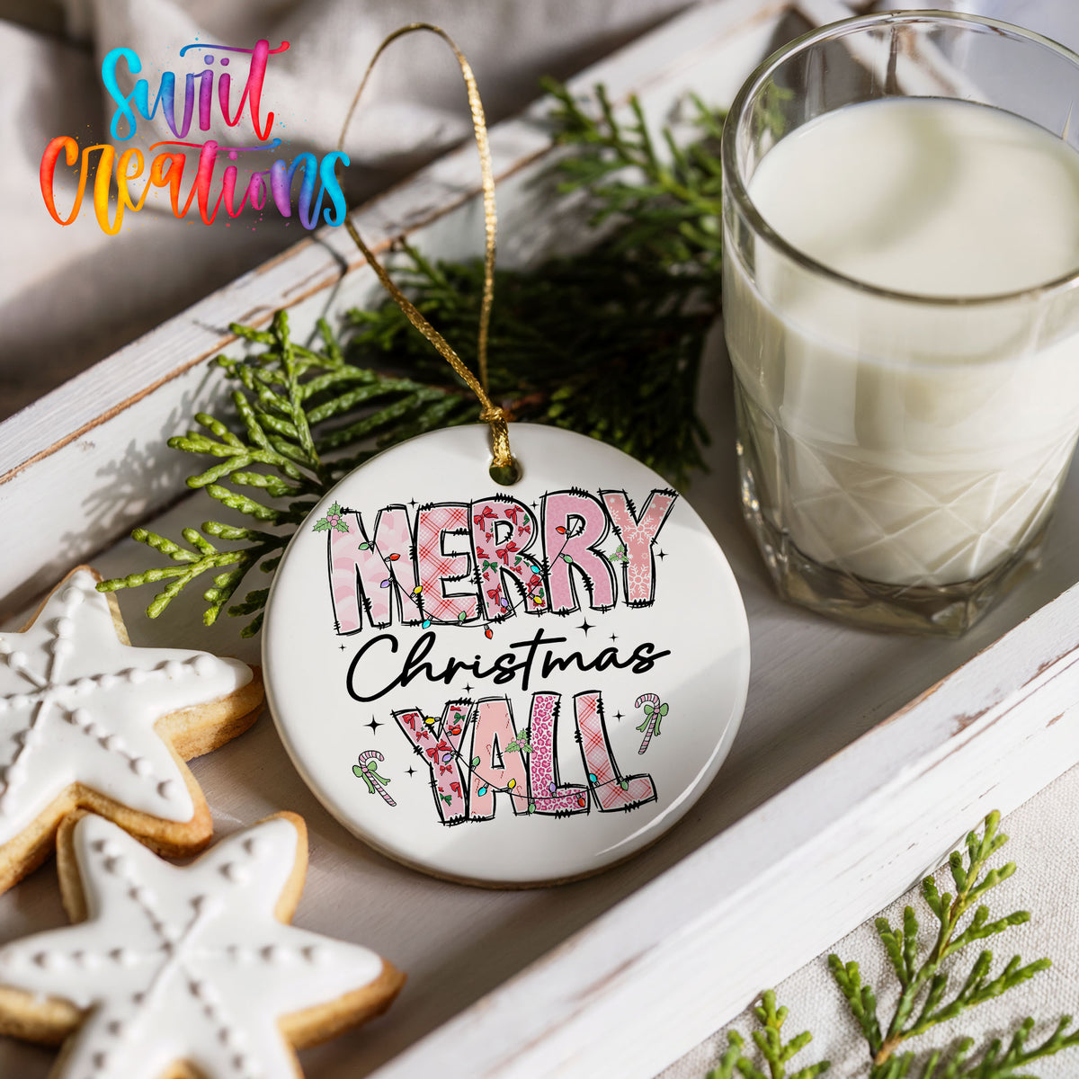 Round ceramic Christmas ornament featuring patterned Merry Christmas Y’all lettering with pink and green accents, styled with cookies and milk