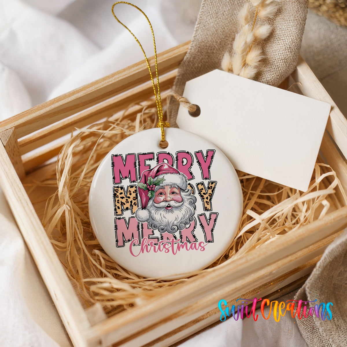Round ceramic Christmas ornament featuring stacked Merry Merry Merry Christmas lettering with Santa and leopard print accents, presented in a rustic wooden gift crate