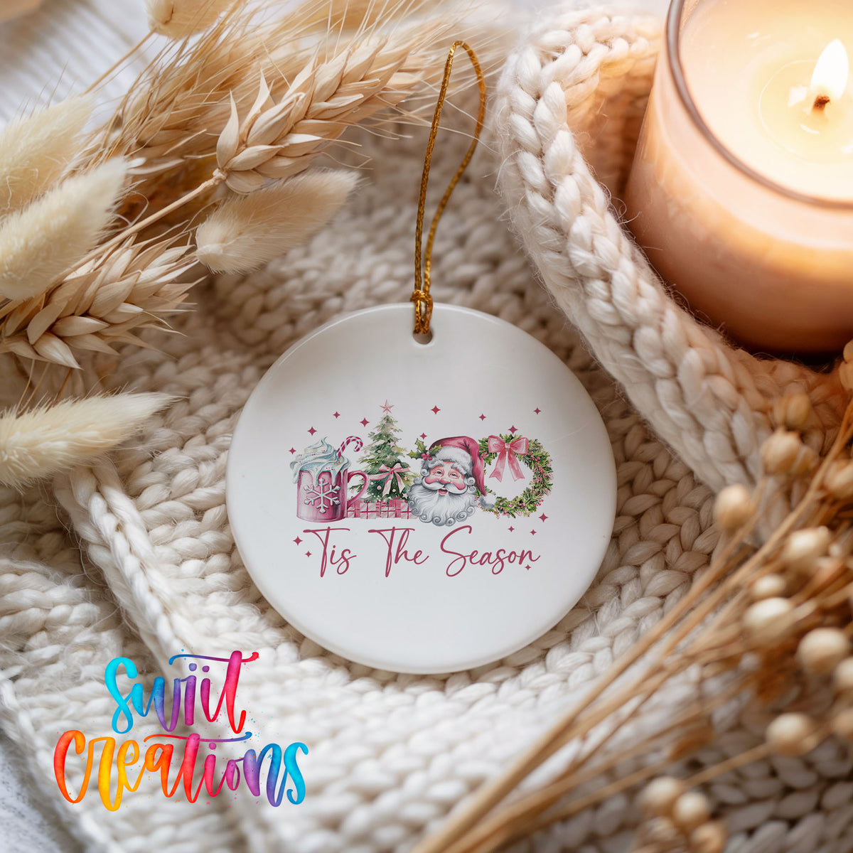 Round ceramic Christmas ornament featuring vintage Santa with floral greenery and ’Tis the Season lettering, styled beside a candle and cozy knit blanket