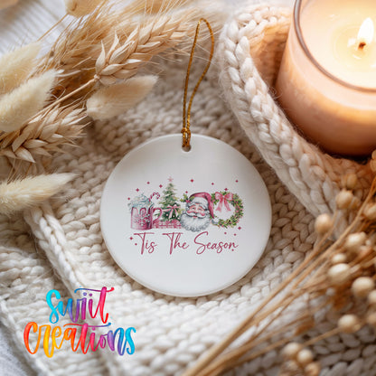 Round ceramic Christmas ornament featuring vintage Santa with floral greenery and ’Tis the Season lettering, styled beside a candle and cozy knit blanket