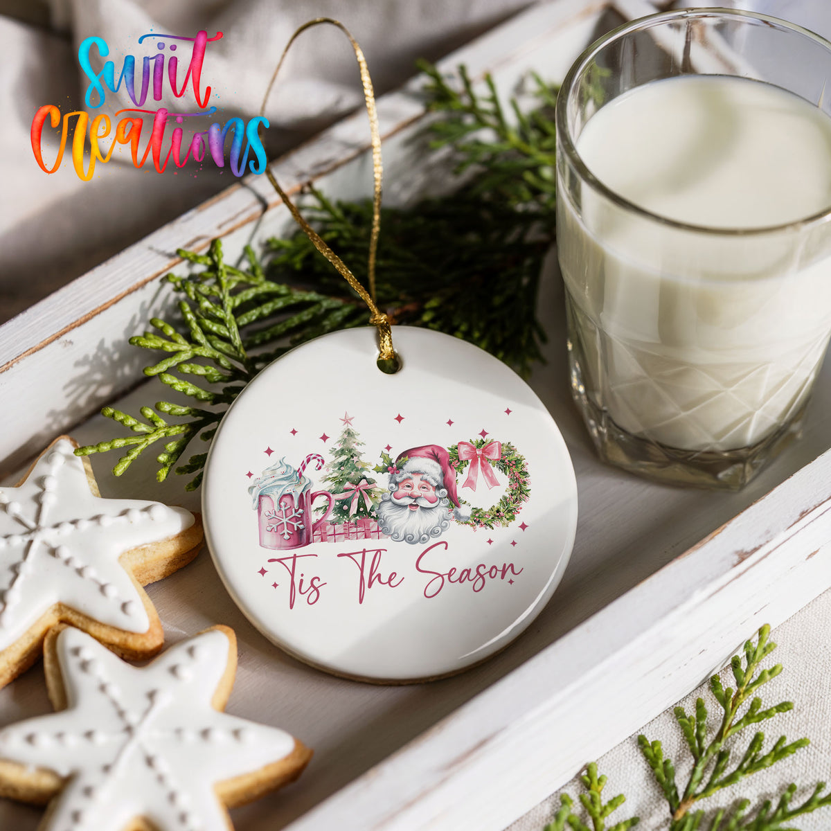 Round ceramic Christmas ornament featuring vintage Santa with floral greenery and ’Tis the Season lettering, styled with cookies and milk