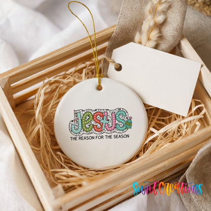 Round ceramic Christmas ornament featuring colorful Jesus Is the Reason for the Season typography, presented in a rustic wooden gift crate