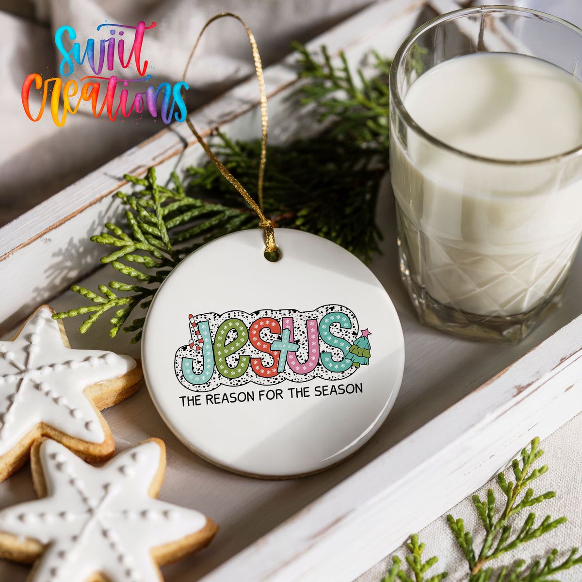 Round ceramic Christmas ornament featuring colorful Jesus Is the Reason for the Season typography, styled with cookies and milk