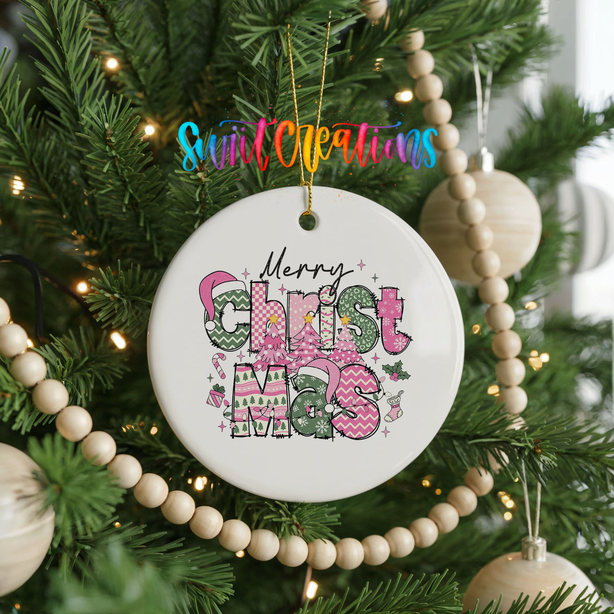 Round ceramic Christmas ornament featuring stacked patterned Merry Christmas lettering in pink green and black, hanging on a decorated Christmas tree