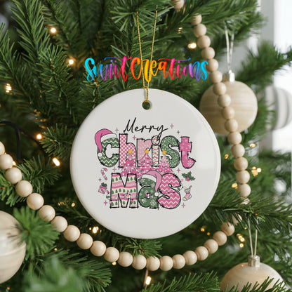 Round ceramic Christmas ornament featuring stacked patterned Merry Christmas lettering in pink green and black, hanging on a decorated Christmas tree