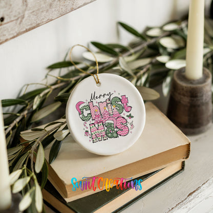 Round ceramic Christmas ornament featuring stacked patterned Merry Christmas lettering in pink green and black, styled on books with holiday greenery