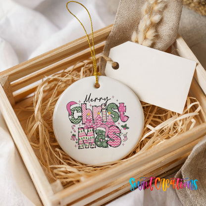 Round ceramic Christmas ornament featuring stacked patterned Merry Christmas lettering in pink green and black, presented in a rustic wooden gift crate