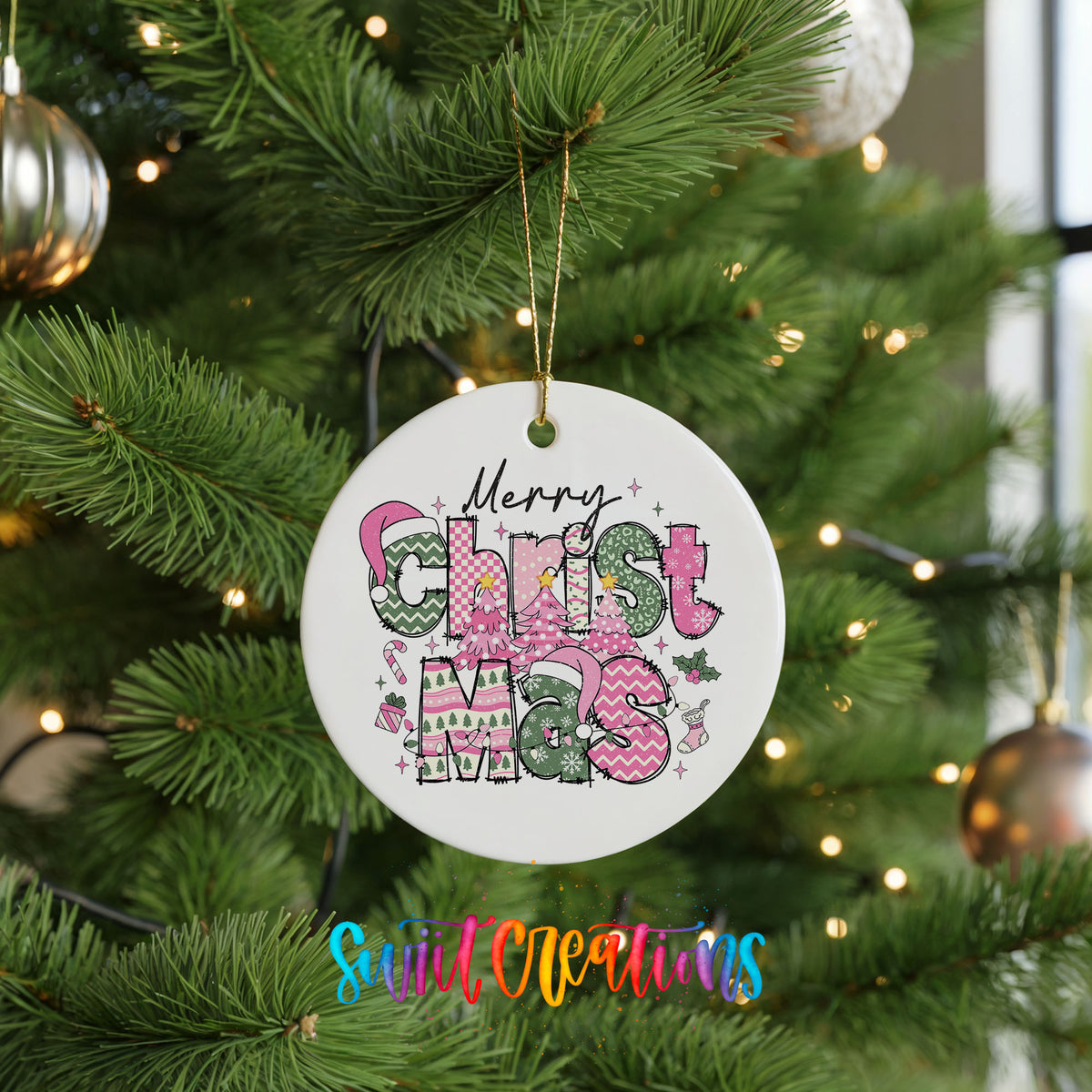 Round ceramic Christmas ornament featuring stacked patterned Merry Christmas lettering in pink green and black, hanging on a green Christmas tree