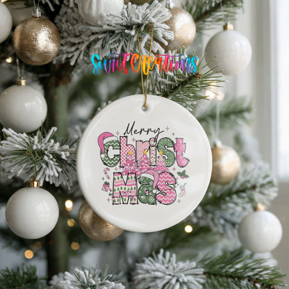 Round ceramic Christmas ornament featuring stacked patterned Merry Christmas lettering in pink green and black, hanging on a frosted holiday tree