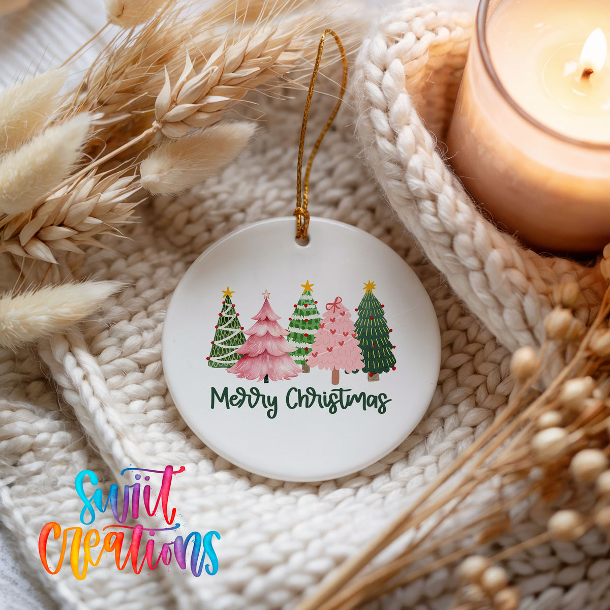 Round ceramic Christmas ornament featuring row of whimsical colorful Christmas trees with Merry Christmas script, styled beside a candle and cozy knit blanket