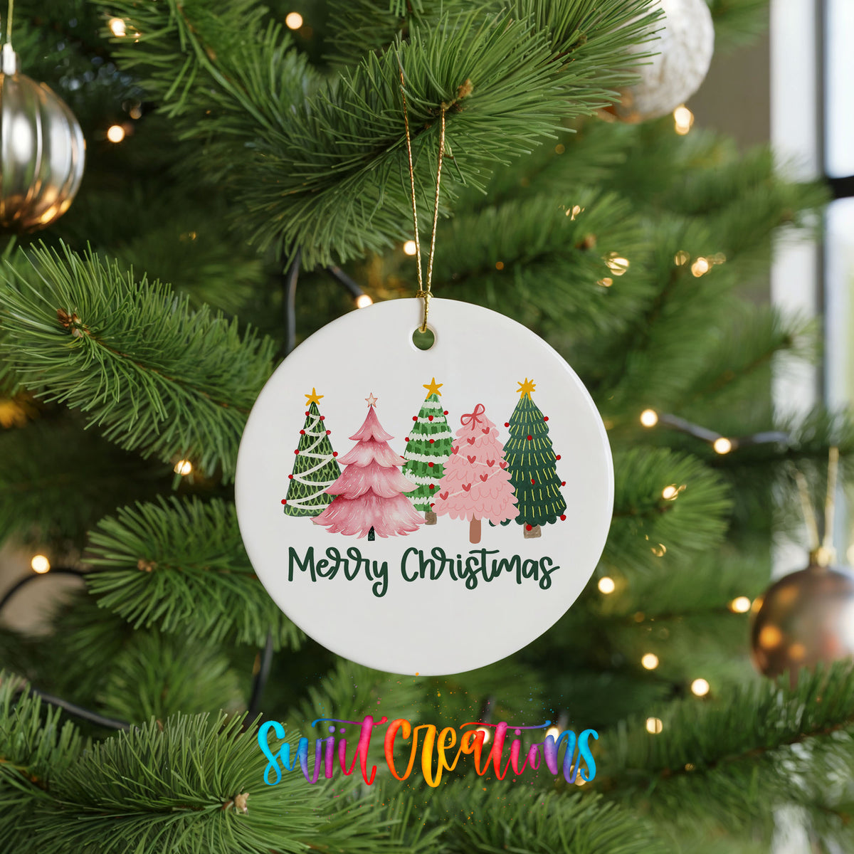 Round ceramic Christmas ornament featuring row of whimsical colorful Christmas trees with Merry Christmas script, hanging on a green Christmas tree