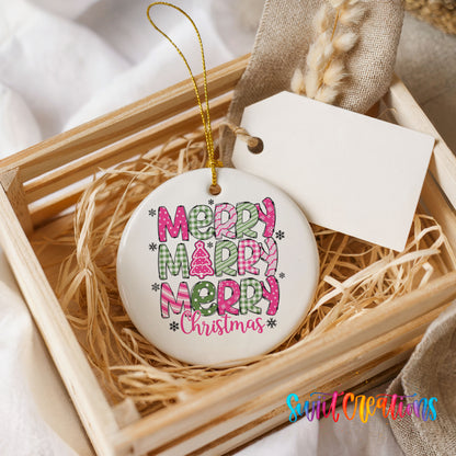 Round ceramic Christmas ornament featuring stacked patterned Merry Merry Merry Christmas lettering in pink and green, presented in a rustic wooden gift crate