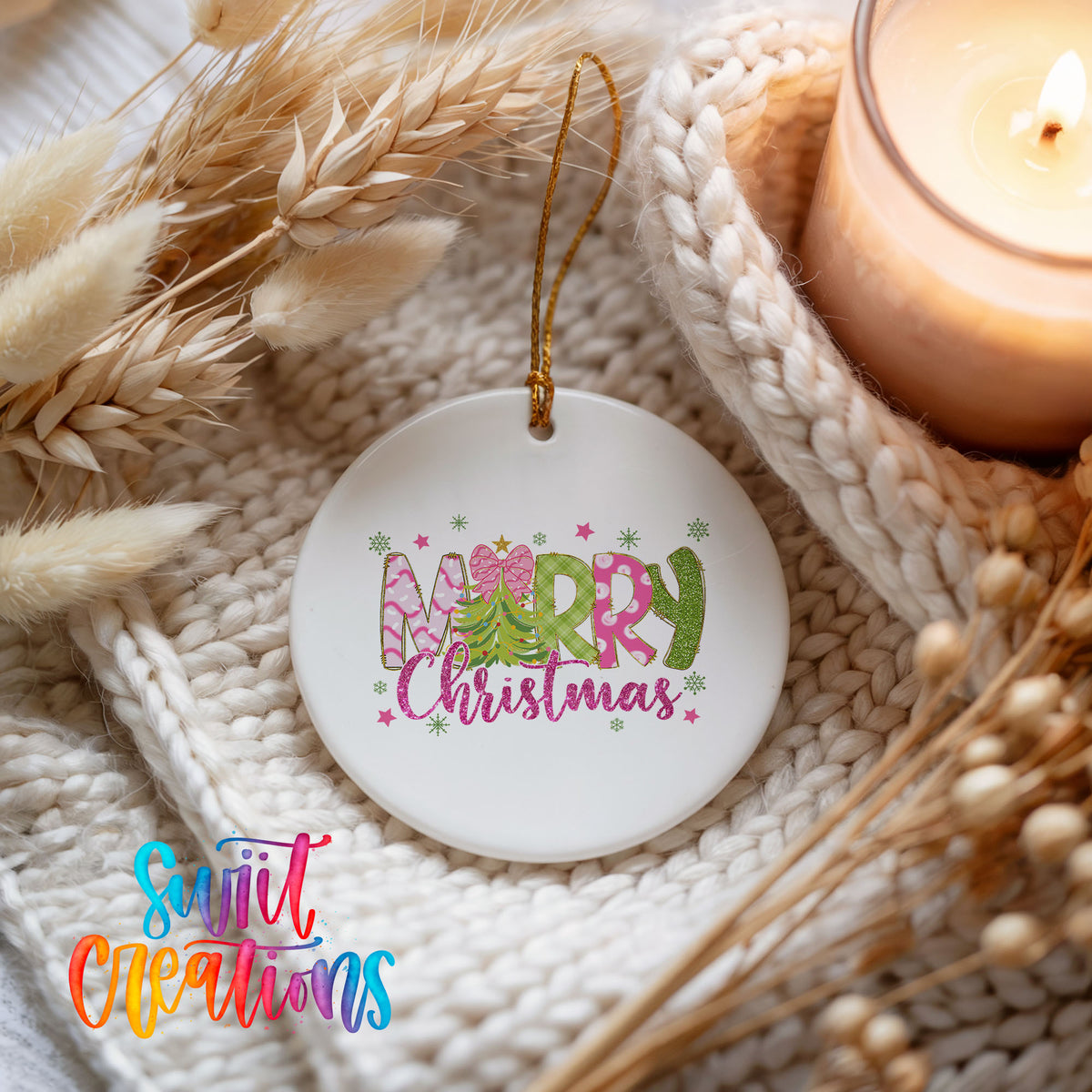 Round ceramic Christmas ornament featuring bright Merry Christmas lettering with candy stripe and floral details, styled beside a candle and cozy knit blanket
