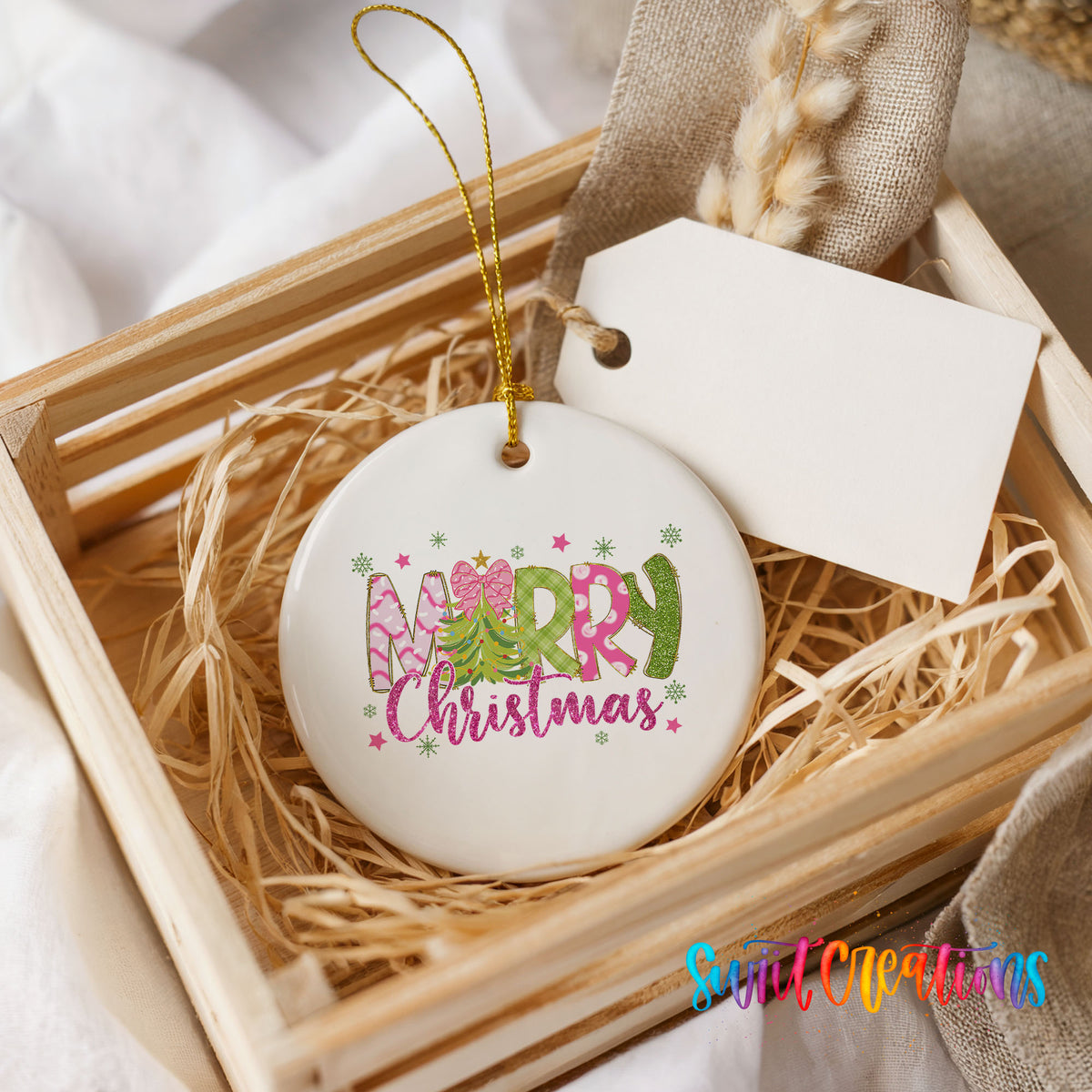 Round ceramic Christmas ornament featuring bright Merry Christmas lettering with candy stripe and floral details, presented in a rustic wooden gift crate