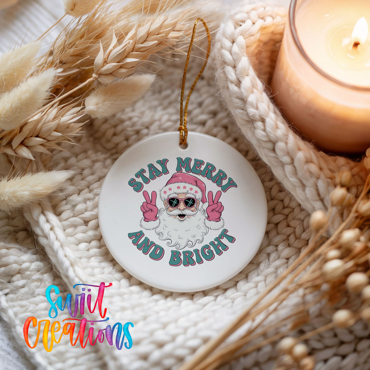Round ceramic Christmas ornament featuring Santa in sunglasses giving peace signs with Stay Merry and Bright lettering, styled beside a candle and cozy knit blanket